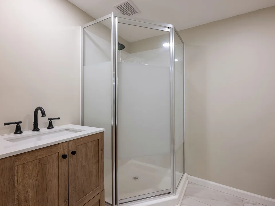 A frosted glass corner shower enclosure beside a wood vanity with a black faucet.