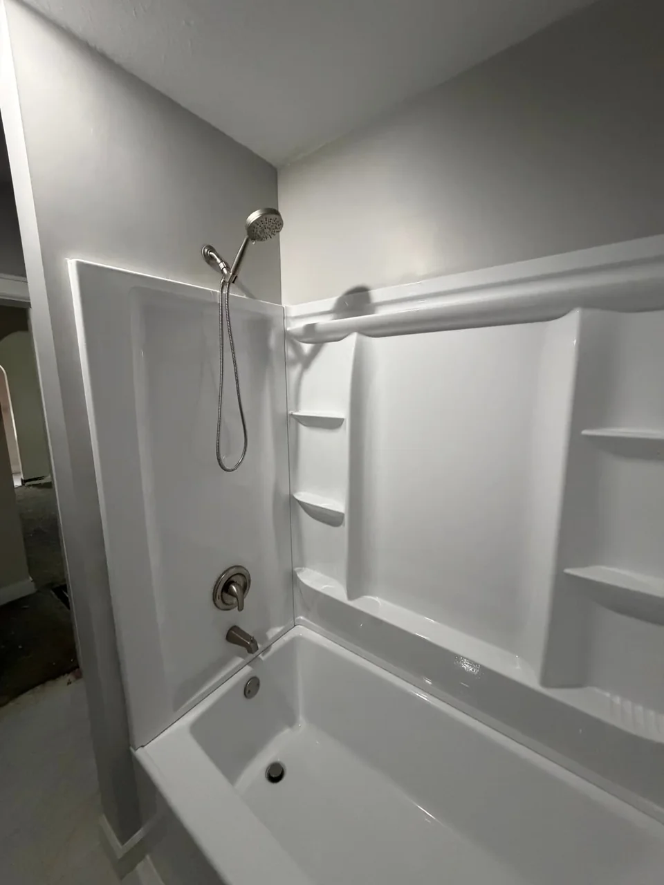 A white tub and shower surround with built-in shelving.